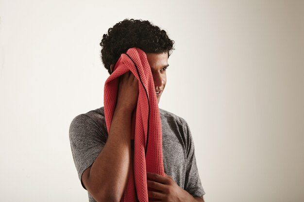 muscular smiling black model in gray running t-shirt wipes the side of his face with a red towel looking away from