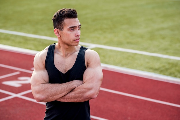 Muscular young sport person with his arm crossed standing on race track