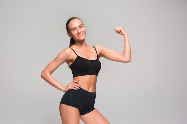 Muscular young woman athlete posing on gray