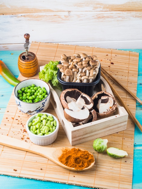 Mushroom; green peas; brussels sprouts; spice; and spice grinder on placemat in kitchen