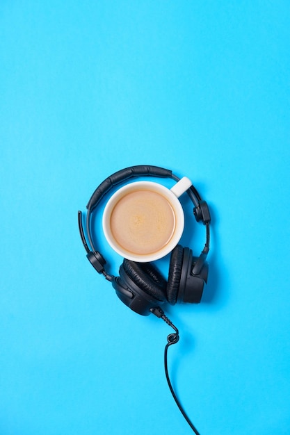 Music or podcast background with headphones and cup of coffee on blue table flat lay Top view flat lay