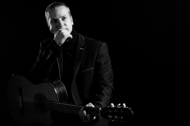 Music. Young musician in black suit holding a guitar