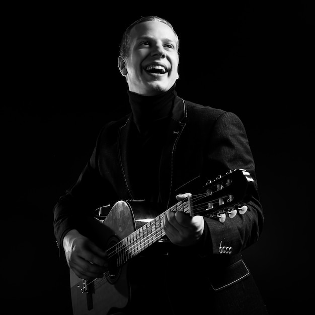 Music. Young musician in black suit holding a guitar