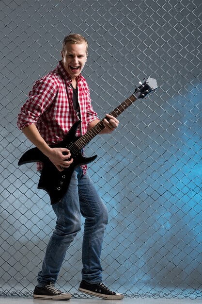 Music. Young musician with a guitar on fence wall