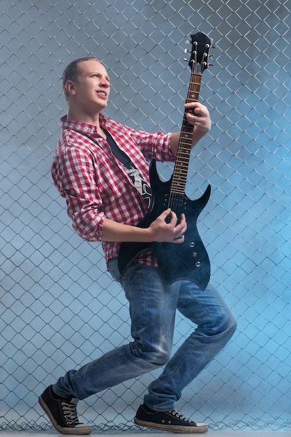 Free photo music. young musician with a guitar on fence wall