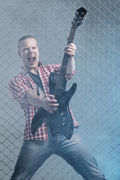 Music. Young musician with a guitar on fence wall