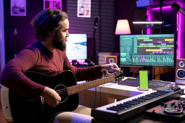 Free photo musician learning to tune his guitar with internet tutorial via greenscreen