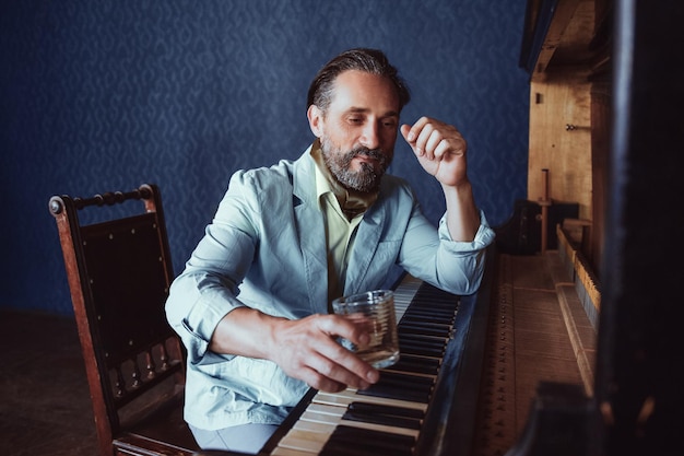 Free photo musician at the piano composes music. in his hand a glass of alcoholic beverage