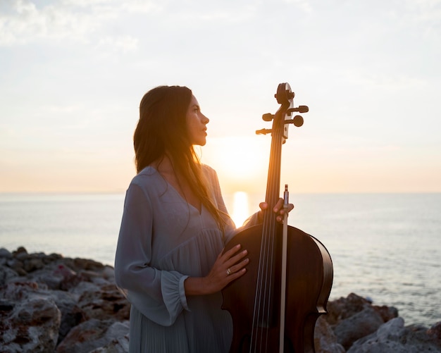 Free photo musician with cello outdoors at sunset