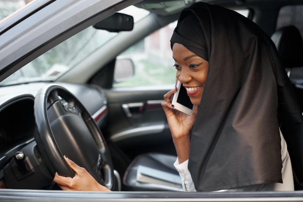 Muslim woman sitting in car talking by mobile phone