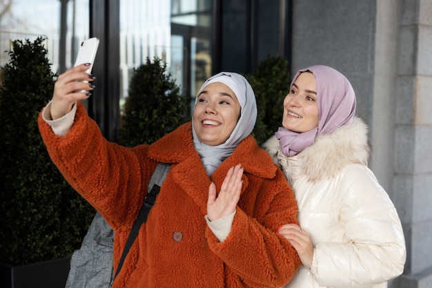 Muslim women with hijabs taking a selfie and waving while being on vacation