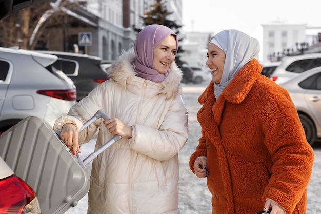 Free photo muslim women with hijabs taking their luggage out of a car's trunk while being on vacation