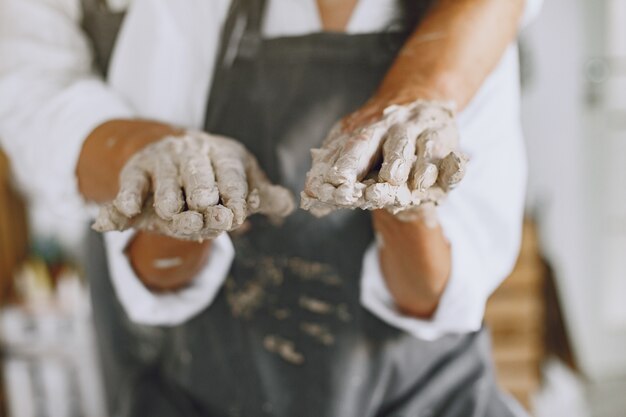 Mutual creative work. Adult elegant couple in casual clothes and aprons. People creating a bowl on a pottery wheel in a clay studio.