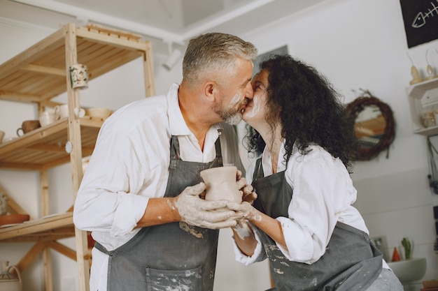 Free Photo mutual creative work. adult elegant couple in casual clothes and aprons. people creating a bowl on a pottery wheel in a clay studio.