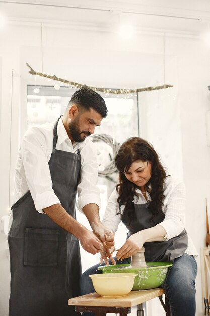 Mutual creative work. Elegant couple in casual clothes and aprons. People creating a bowl on a pottery wheel in a clay studio.