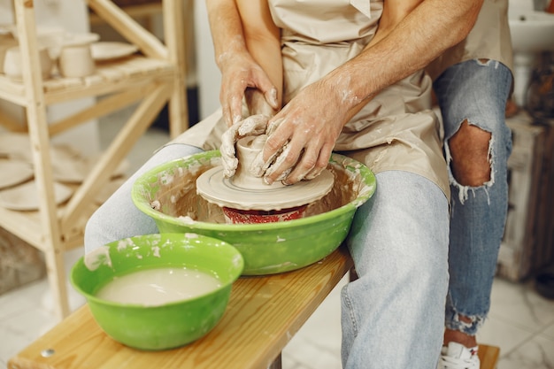 Free photo mutual creative work. young beautiful couple in casual clothes and aprons. people creating a bowl on a pottery wheel in a clay studio.