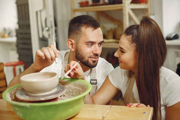 Free Photo mutual creative work. young beautiful couple in casual clothes and aprons. people creating a bowl on a pottery wheel in a clay studio.