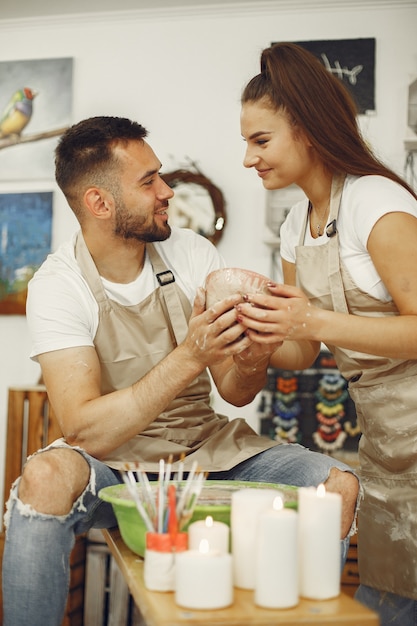 Free photo mutual creative work. young beautiful couple in casual clothes and aprons. people creating a bowl on a pottery wheel in a clay studio.