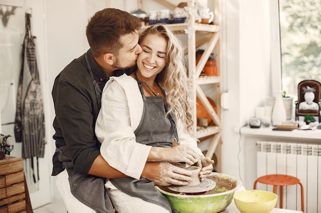 Free Photo mutual creative work. young beautiful couple in casual clothes and aprons. people creating a bowl on a pottery wheel in a clay studio.