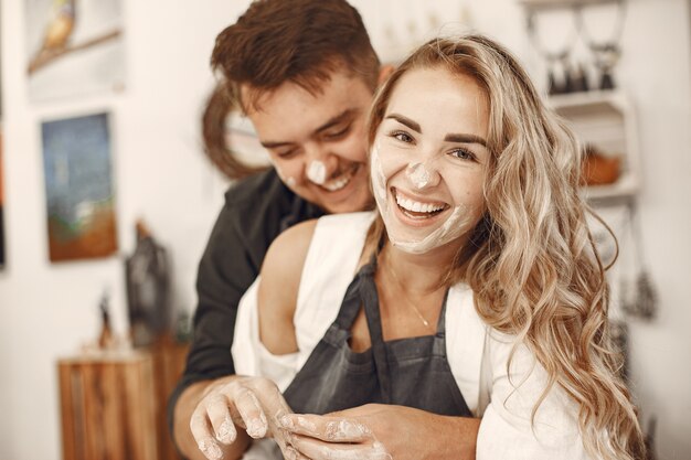 Mutual creative work. Young beautiful couple in casual clothes and aprons. People creating a bowl on a pottery wheel in a clay studio.