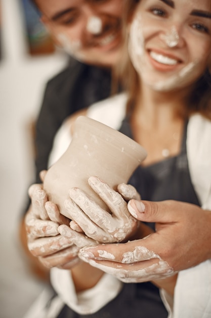 Free photo mutual creative work. young beautiful couple in casual clothes and aprons. people creating a bowl on a pottery wheel in a clay studio.