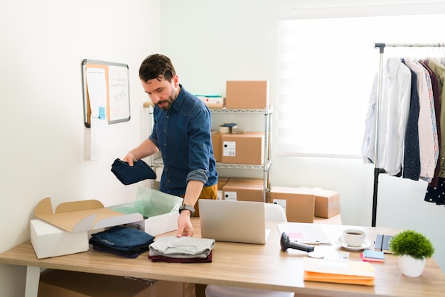 My online clothing store is growing. Handsome business owner putting t-shirts on boxes and arranging packages to ship to his customers