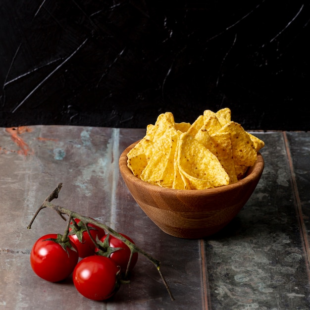 Free photo nachos in bowl and branch of tomatoes on table