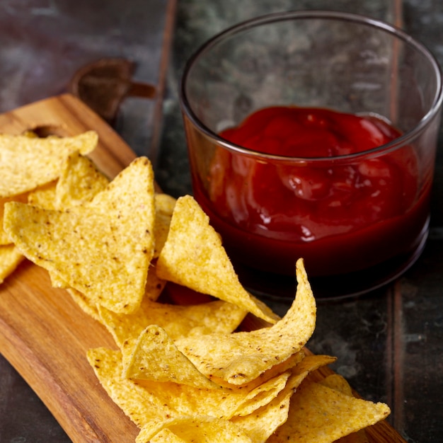 Free Photo nachos on cutting wooden board and tomato sauce in bowl