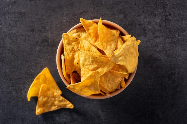 Nachos in wooden bowl on black slate background