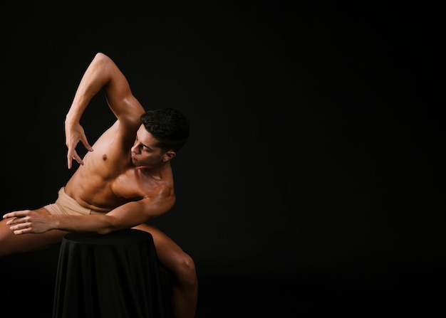 Naked man leaning with elbow on chair and raising hand