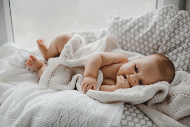 Free photo naked newborn boy lies on the soft blanket before a bright window