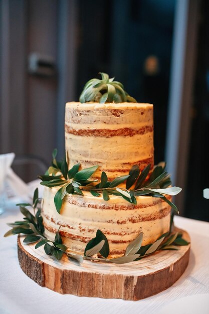 Naked rustic wedding cake decorated with leaves on wooden cake tier