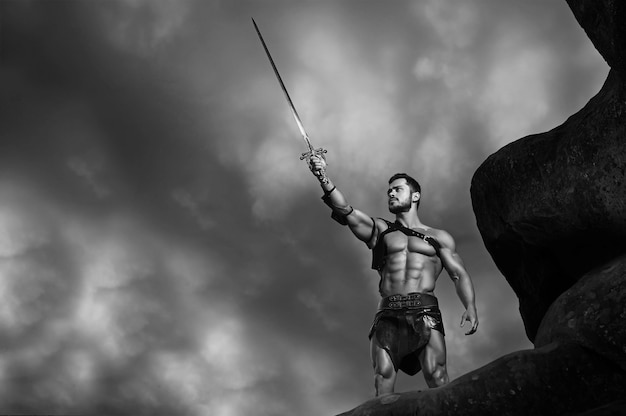 Free Photo in the name of god. monochrome portrait of a powerful muscular gladiator holding his sword up to the stormy sky copyspace