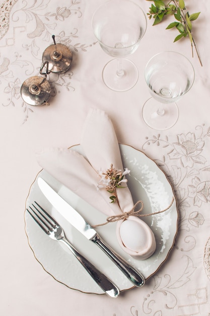 Napkin and cutlery on plate near glasses and plant 