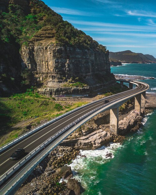 A narrow curvy road with cars alongside green mountains