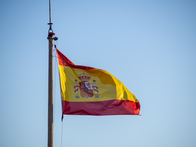 National flag of Spain waving on the flagpole over a clear blue sky