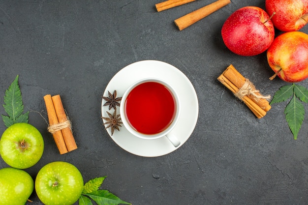 Natural organic fresh apples with green leaves cinnamon limes and a cup of black tea on black background