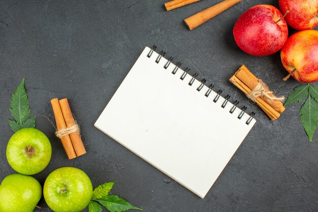 Natural organic fresh apples with green leaves cinnamon limes and notebook on black background