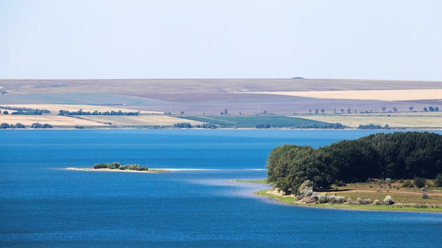 Free photo nature of moldova, lake with small island, meadow with lush trees on the right, wide fields visible in the distance