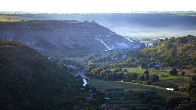 Nature of Moldova, vale with flowing rivers, lush trees along them, fields and rare buildings, rocky hills