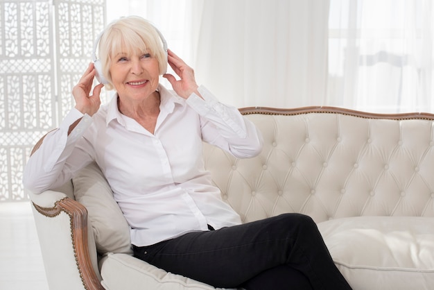 Neat old woman sitting on sofa with headphones