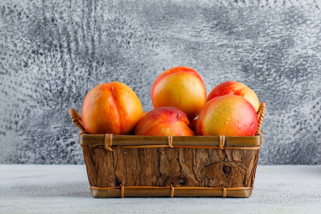 Free photo nectarines in a basket side view on a grungy wall