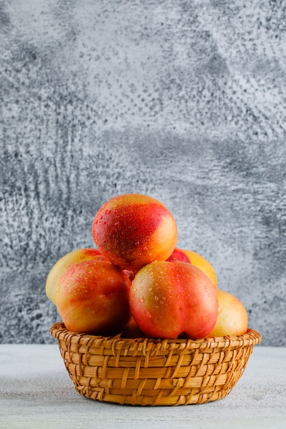 Free photo nectarines in a basket side view on grungy and white wall