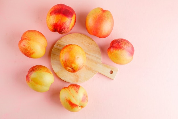 Free photo nectarines on pink and cutting board table. flat lay.