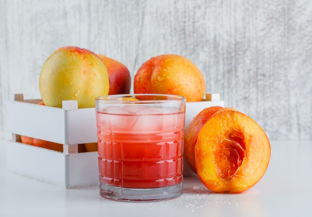 Nectarines in a wooden box with juice side view on white and grungy wall