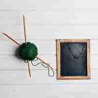 Free photo needles in green wool ball next to chalkboard