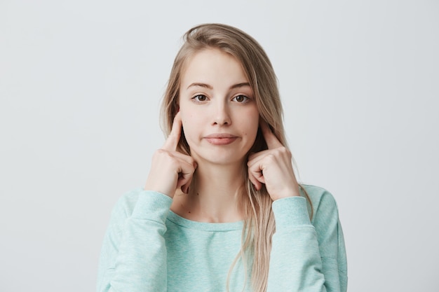 Negative human emotions, reaction and attitude. Frustrated annoyed woman with blonde dyed hair plugging ears with fingers, feeling irritated with loud annoying noise, can't concentrate on work