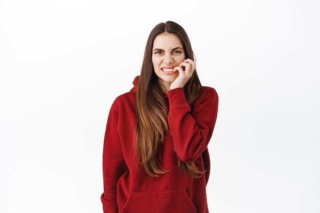 Nervous young woman with bad habits biting fingernails and looking worried anxious or concerned about something looking at camera standing against white background