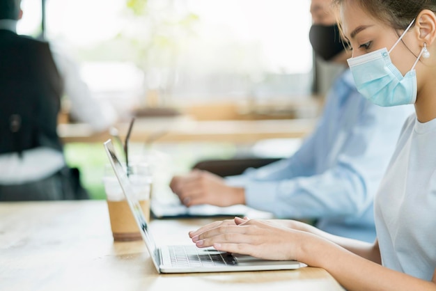 Free Photo new normal lifestyle concept business people wearing mask sit with social distancing working in public area or co working space with laptop and smartphone