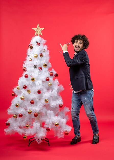 New year celebration with bearded young man drinking wine and standing near decorated white Christmas tree